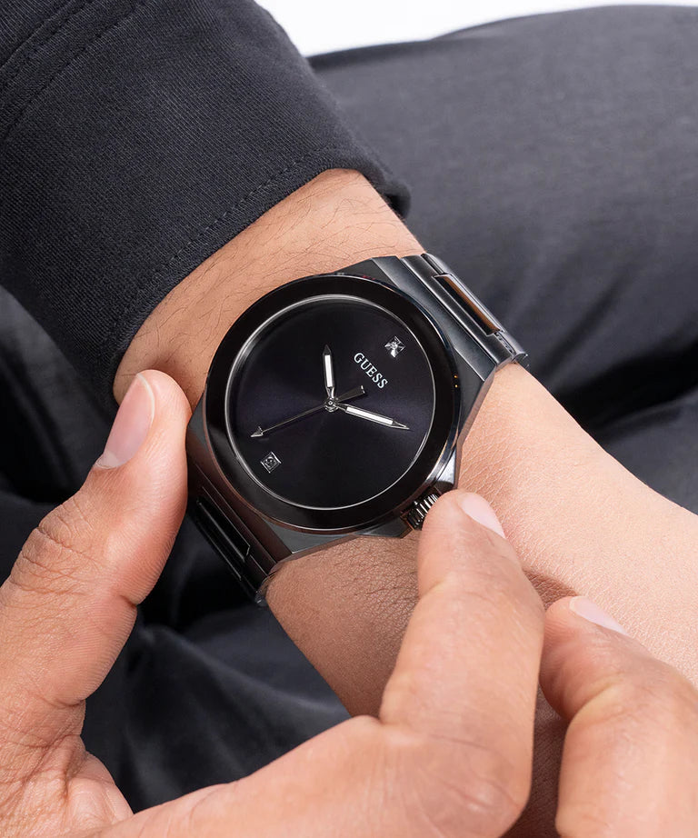 GUESS GW0833G2 watch held in hand showing black dial and gunmetal bracelet detail