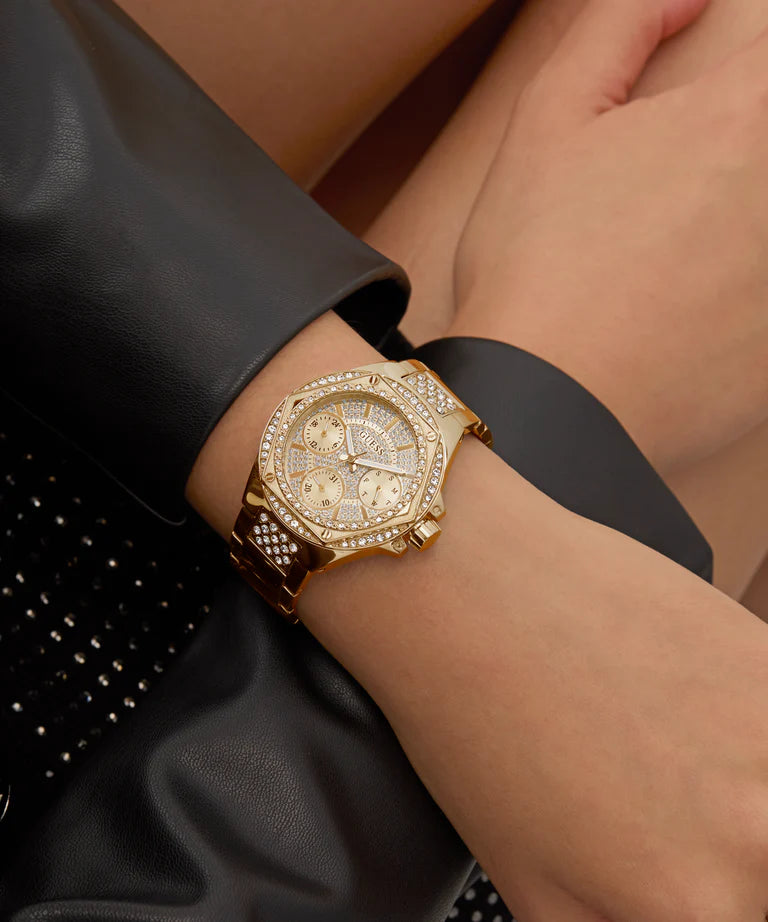 GUESS gold-tone multi-function watch worn on wrist with crystal bezel