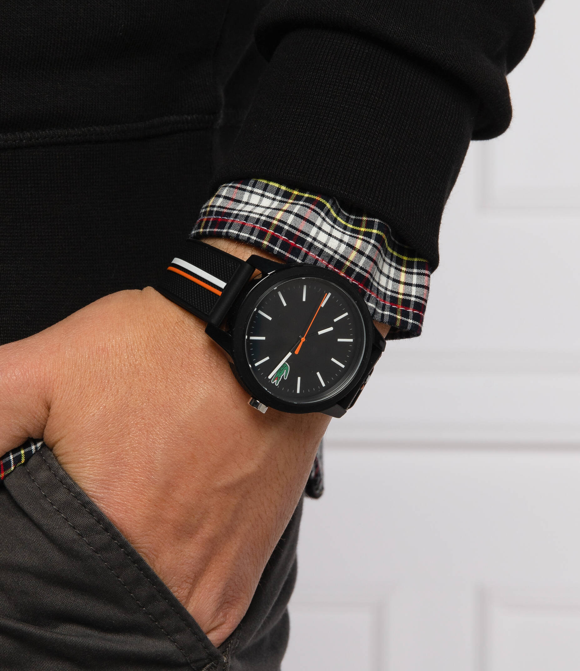 Lacoste 2011071 watch worn on wrist showing black dial and striped strap against plaid fabric