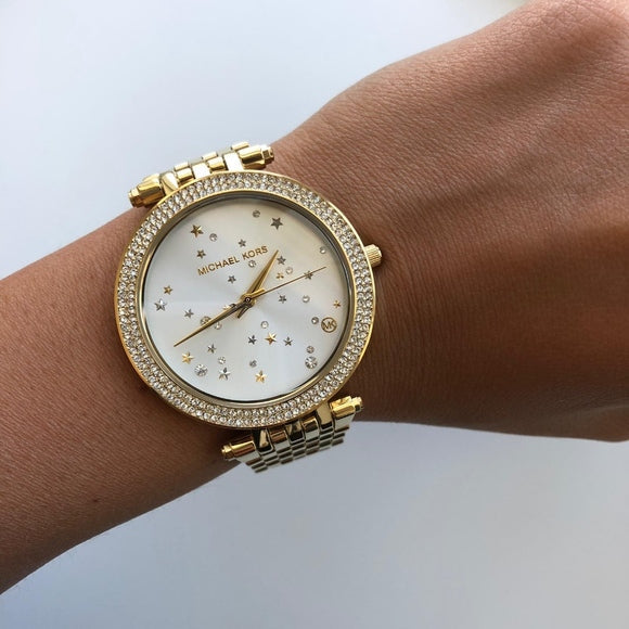 Michael Kors Darci gold watch worn on wrist with crystal bezel and white dial