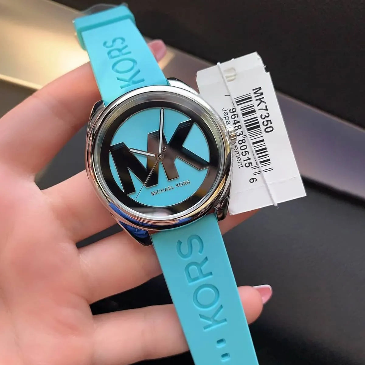 Michael Kors Janelle MK7350 being held showing MK logo dial and turquoise strap with product tag