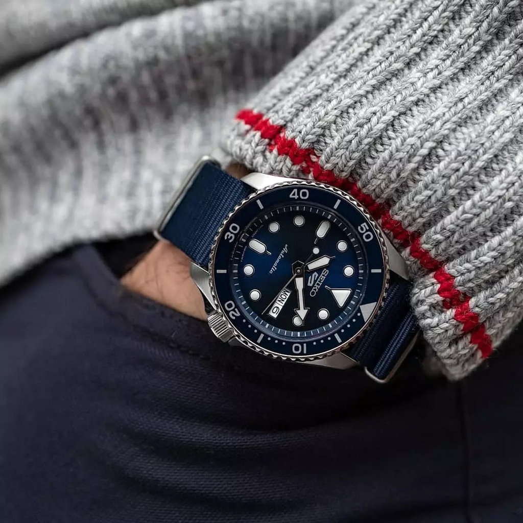 Seiko 5 Sports SRPD51K2 worn on wrist with navy strap, blue dial visible on gray sleeve