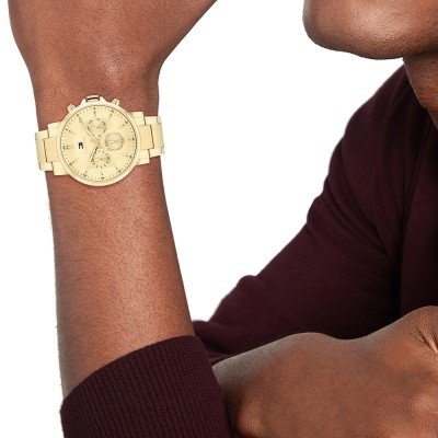 Tommy Hilfiger gold chronograph watch worn on wrist with burgundy shirt sleeve