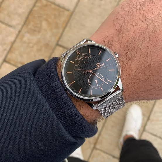 Tommy Hilfiger black dial watch worn on wrist with stainless steel mesh band