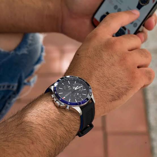 Tommy Hilfiger watch worn on wrist showing black dial, blue bezel, and black rubber strap