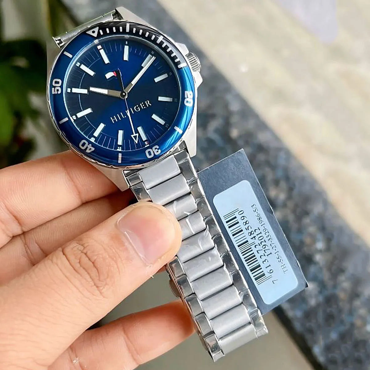 Tommy Hilfiger Logan watch held in hand showing blue dial and silver bracelet with tag