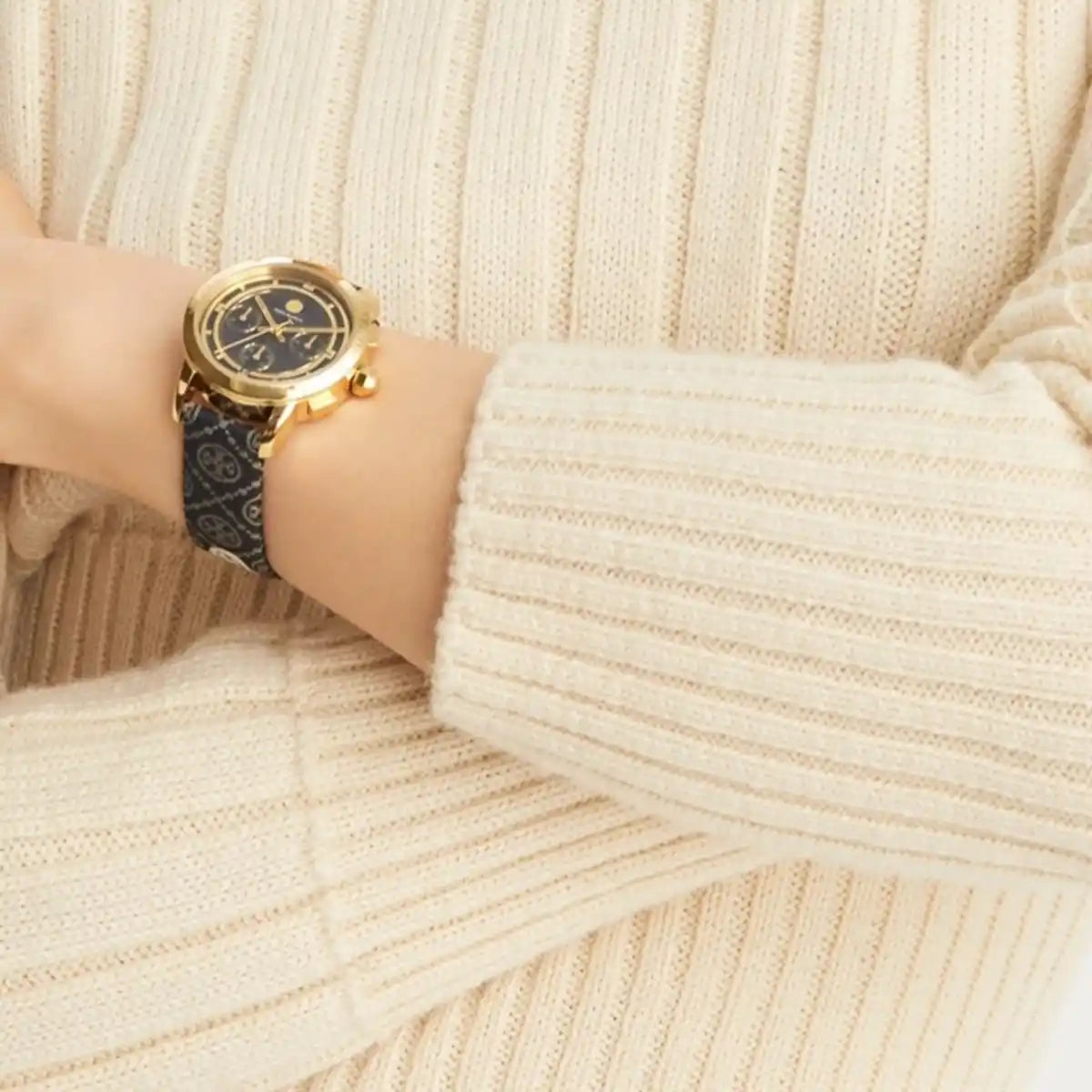 Gold-tone chronograph watch with black monogram jacquard leather strap worn on wrist
